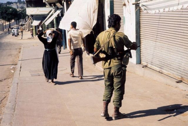 An Israeli solder in a Gaza street while civilians walk nearby