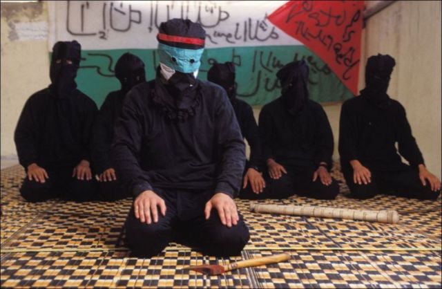 Hamas men kneeling in front of a Palestinian flag