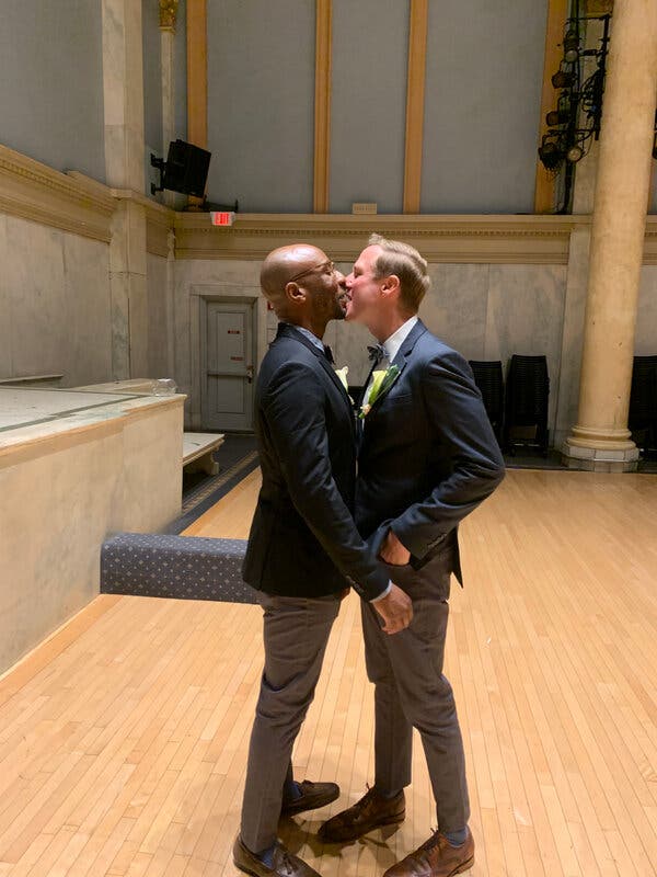 Two men in suits kiss.