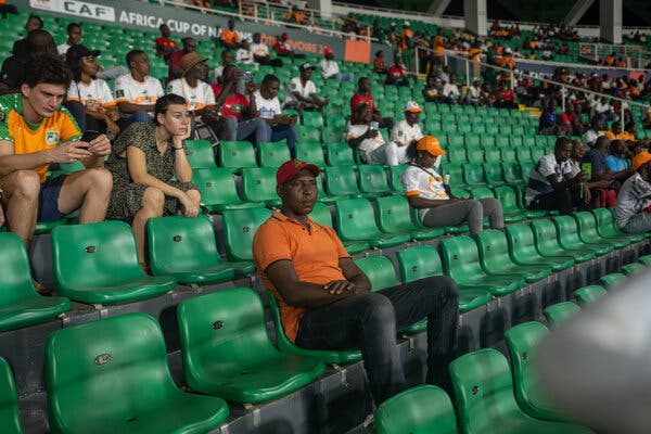 A man sits alone in a row of mostly empty, green stadium seats. 