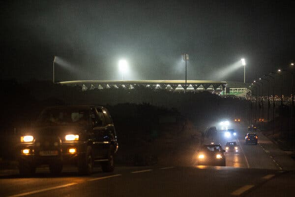 A stadium lit up at night as cars drive past. 