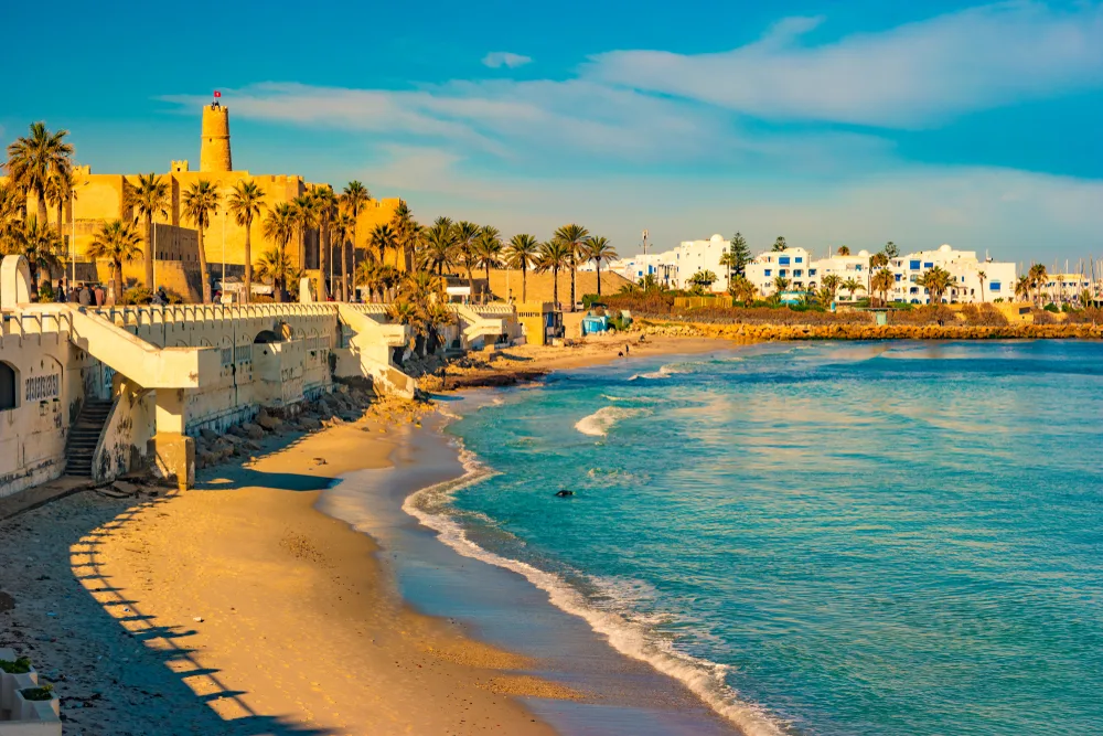 Coastal town of Tunisia pictured at dusk with waves lapping the walled city and a small beach as one of our top picks for places to visit in Africa