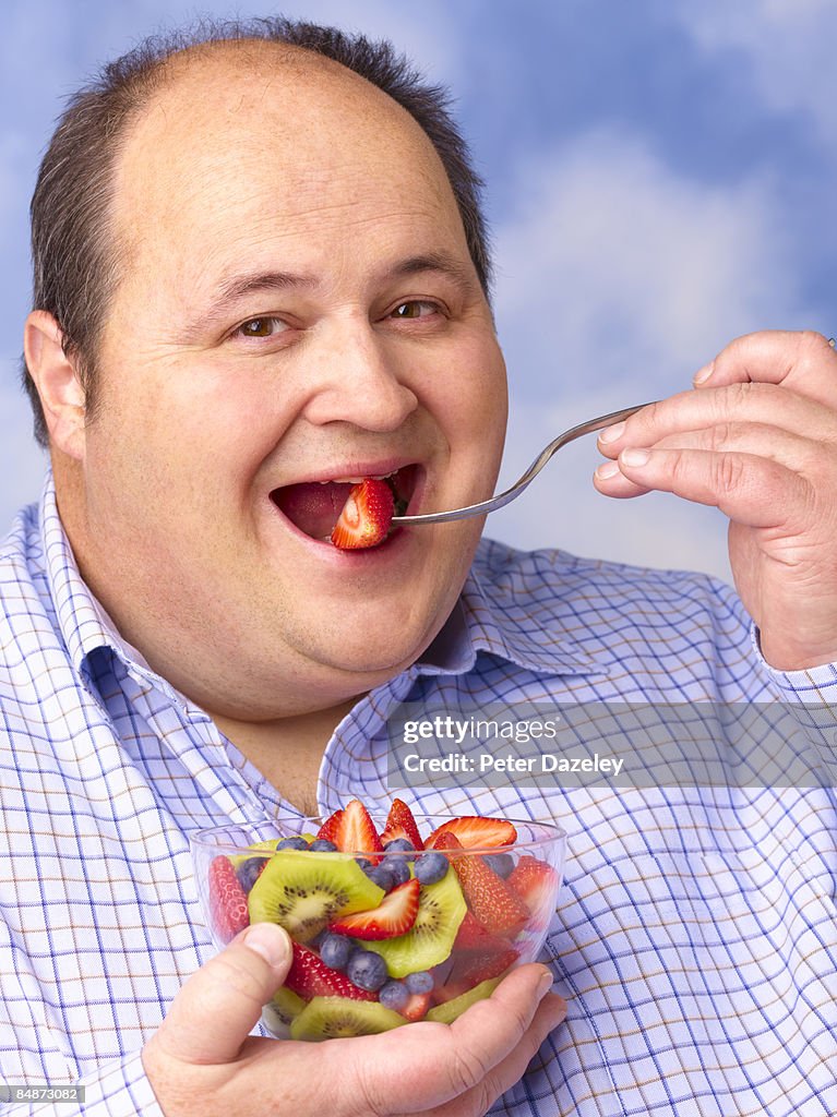 obese-man-eating-fruit-salad-against-sky-picture-id84873082