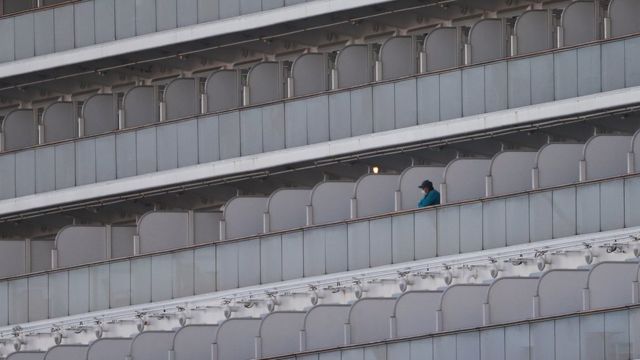 Someone wearing a face mask stands on the balcony of the quarantined Diamond Princess cruise ship