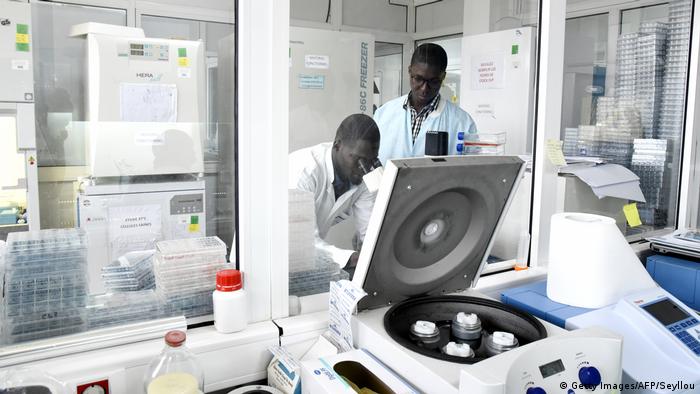 A technician in a white lab coat looks through a microscope