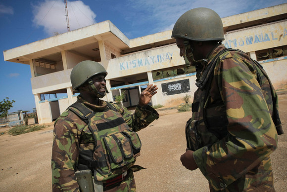 Soldiers of the Kenyan Contingent serving with the African Union Mission in Somalia (AMISOM) stand in front of the black flag of the Al Qaeda-affiliated extremist group Al Shabaab painted on the wall of Kismayo Airport. On 02 October 2012, Kenyan AMISOM troops supporting forces of the Somali National Army and the pro-government Ras Kimboni Brigade moved into and through Kismayo, the hitherto last major urban stronghold of the Al-Qaeda-affiliated extremist group Al Shabaab, on their way to the city's airport without a shot being fired following a month long operation to liberate towns and villages across southern Somalia from Afmadow and Kismayo itself. AU-UN IST PHOTO / STUART PRICE.