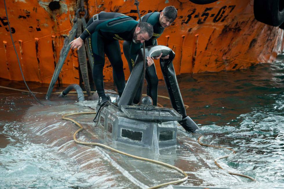 Spanish Civil Guard divers stand over the refloated prow of the submersible.