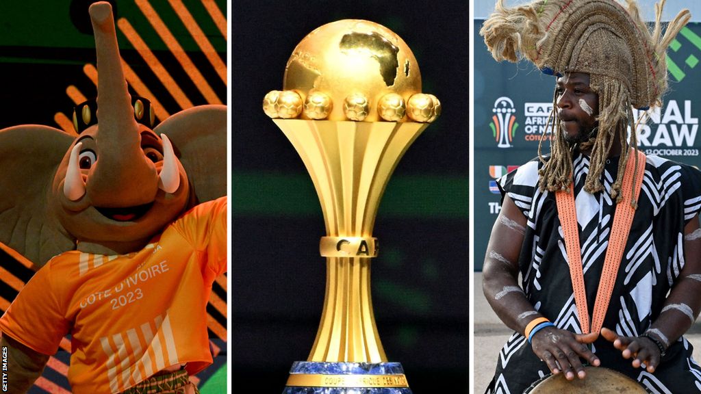 Akwaba, the mascot of the Africa Cup of Nations and a drummer flank the Nations Cup trophy ahead of the draw for the 2023 finals in Ivory Coast