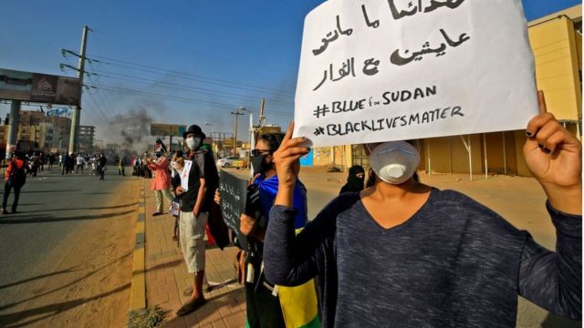 A Sudanese protester holds up a sign reading in Arabic our martyrs are not dead, they are alive with the revolutionaries along with the English slogans #BLUEforSUDAN and #BLACKLIVESMATTER, as demonstrators mark the first anniversary of a raid on an anti-government sit-in and some demonstrate in support of US protesters over the death of George Floyd, in the Riyadh district in the east of the capital Khartoum on June 3, 2020