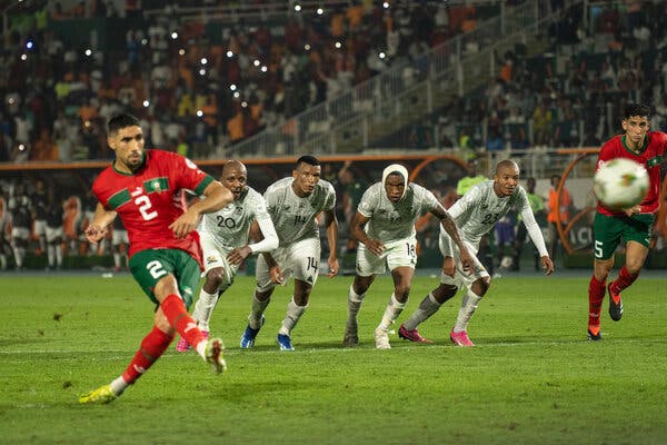 A soccer player kicks the ball while opposing team members react. 