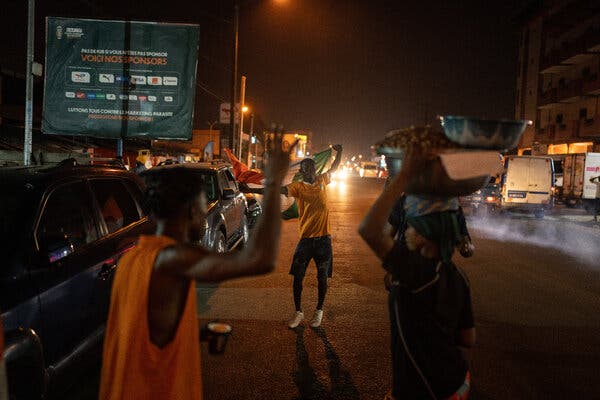 A soccer fan hoists a flag overhead and dances in the street while others watch. 