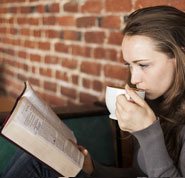 Photo of a woman, drinking a cup of coffee and reading the Bible, in order to know the God who exists on a personal level.