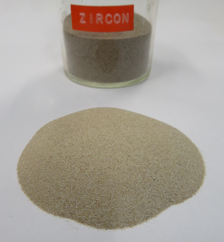 A pile of fine white sand sits in front of a glass jar of sand. The jar is labelled zircon.